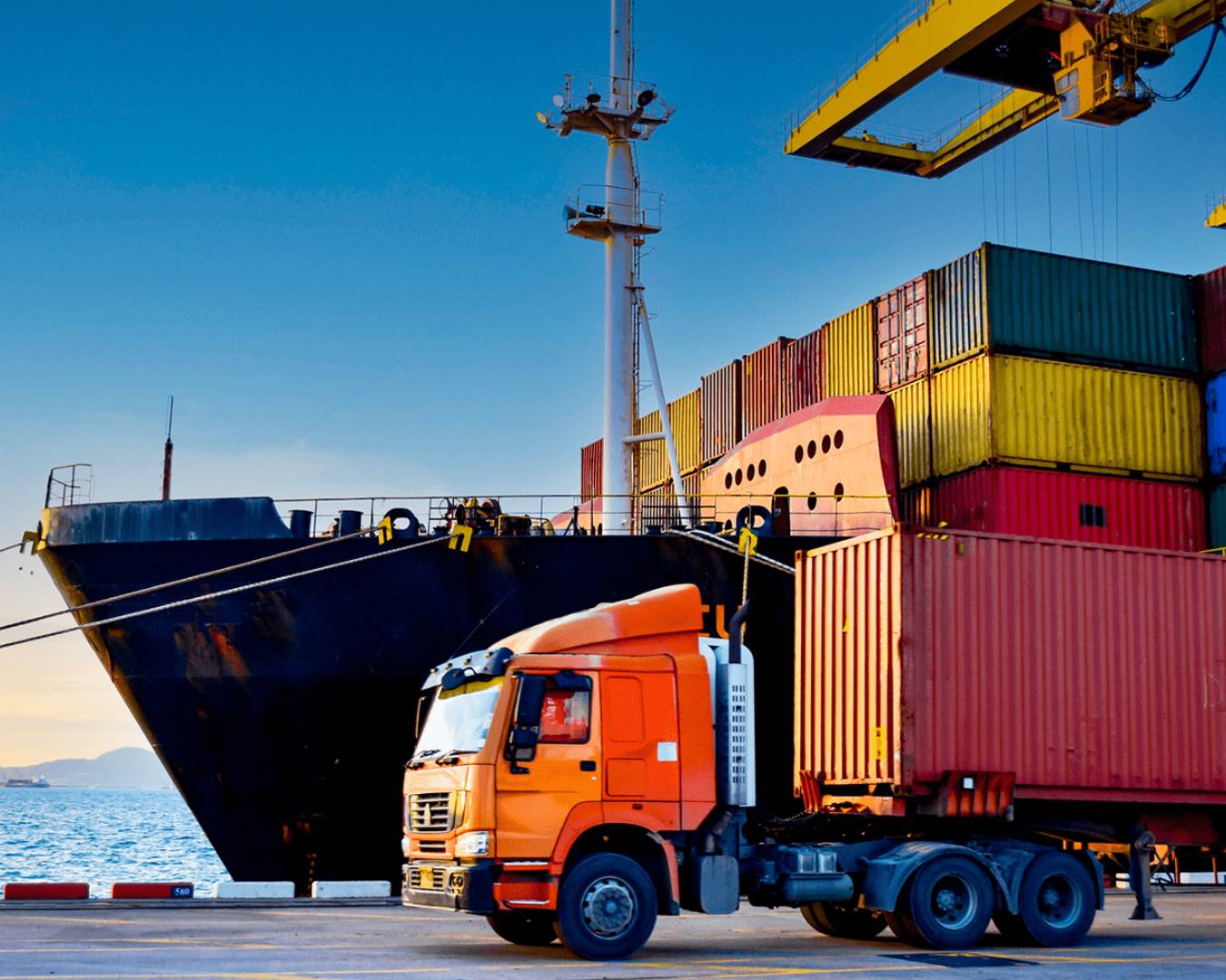 Orange truck beside container ship at port